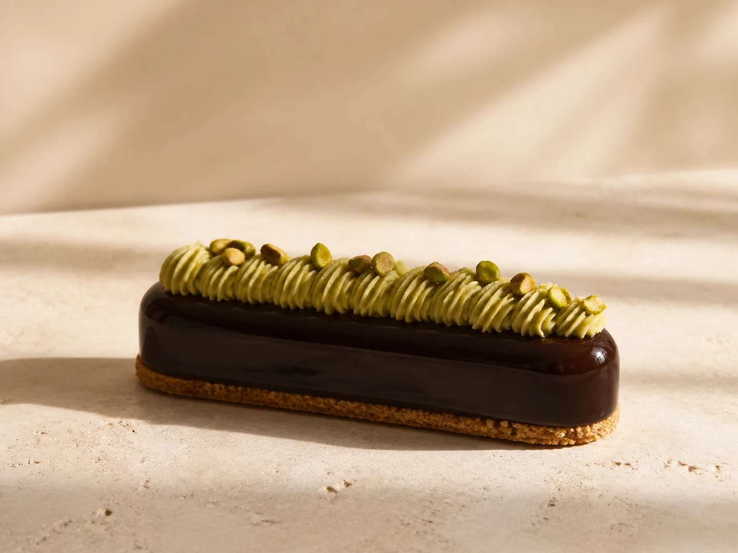 Entremets signature au chocolat brillant, crème pistache et sablé aux amandes.